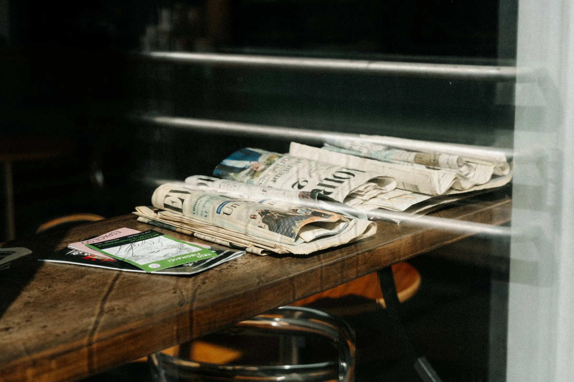 A stack of newspapers resting on a cafe table in Montreal, Quebec. Sunlight creating shadows.